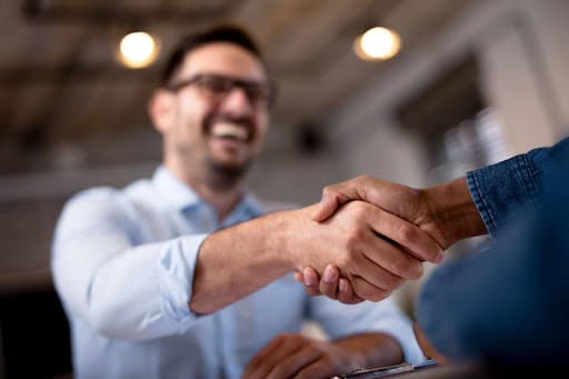 A man in a white shirt shakes the hand of someone wearing a denim jacket